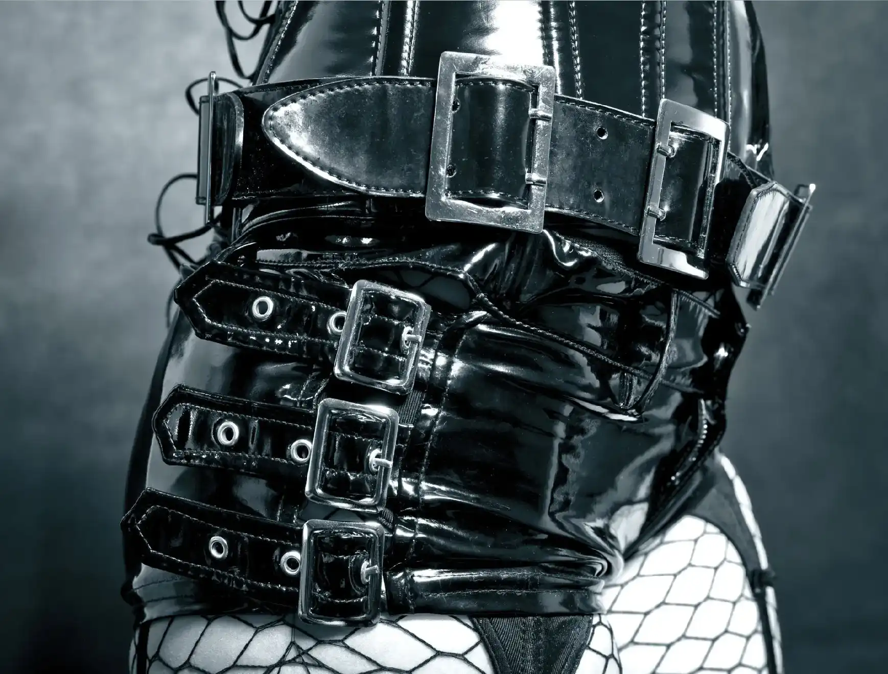 Close-up of shiny black leather straps with buckles and fishnet stockings.