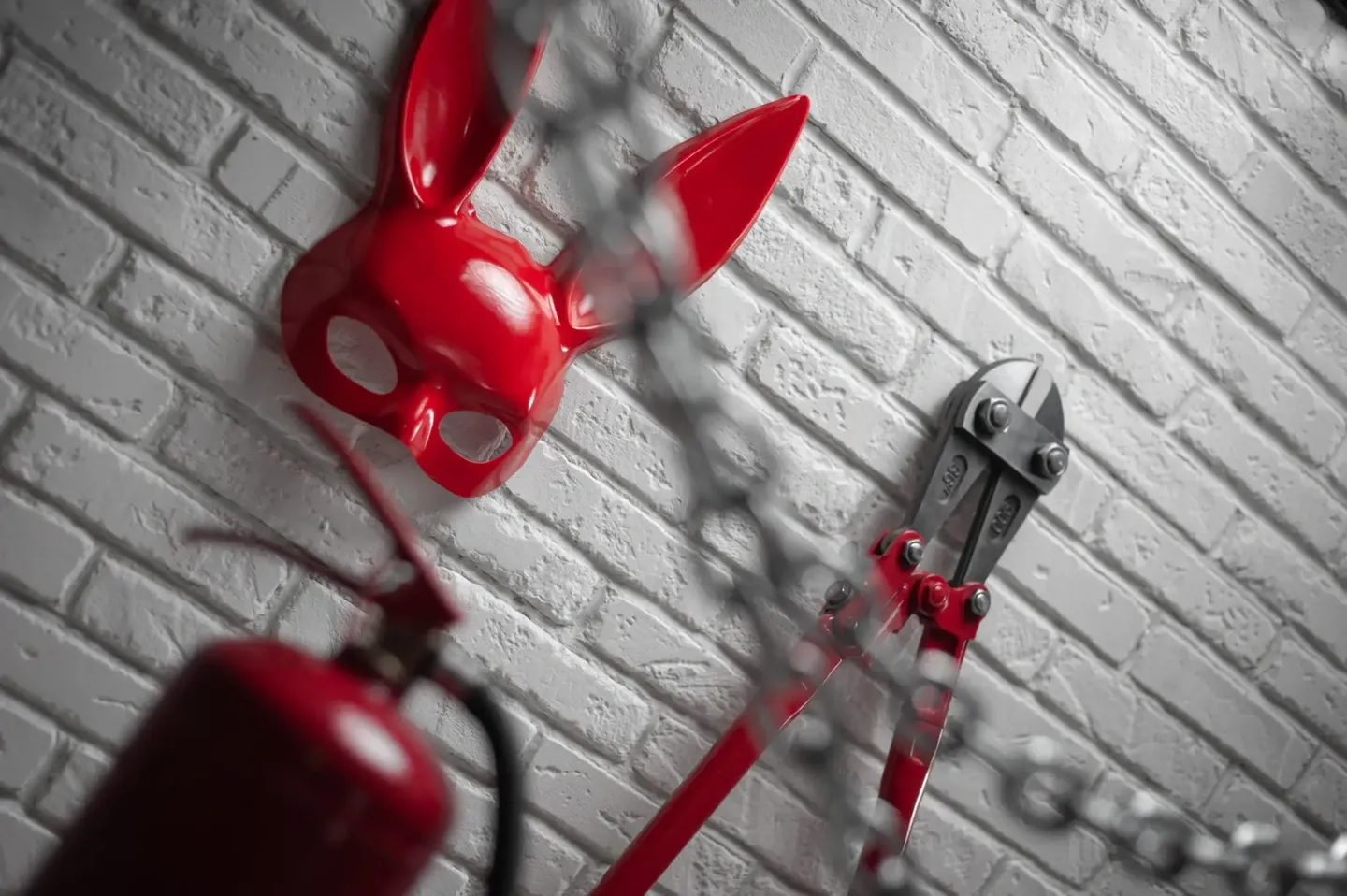 Red superhero mask and tools hanging on a grey brick wall.